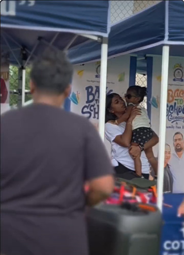 A parent holds a child at the Cottage Home Care Back-to-School Giveback tent, from the maisoneclatworld recap reel.